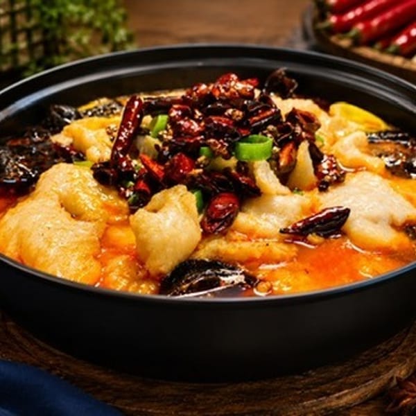 Spicy fish hotpot with chili peppers, mushrooms, and green onions in a black pot.