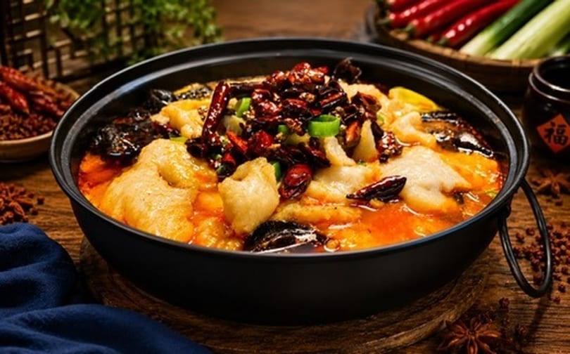 Spicy fish hotpot with chili peppers, mushrooms, and green onions in a black pot.