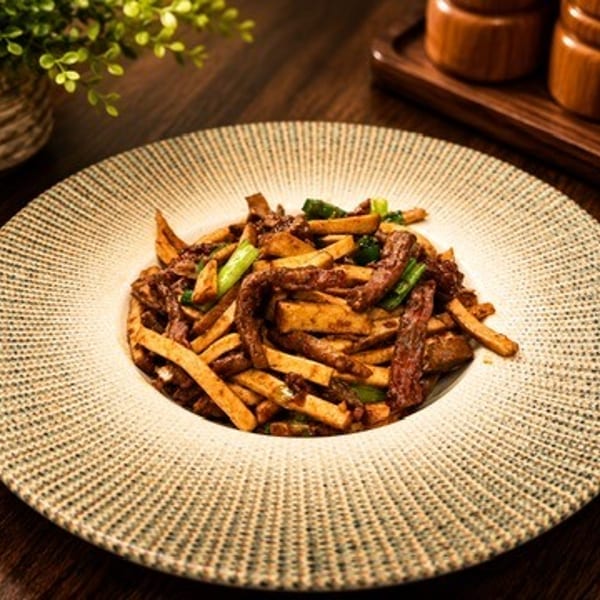 Stir-fried beef and bamboo shoots with green onions on a textured white plate.