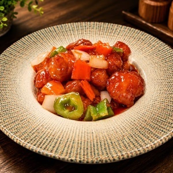 Sweet and sour chicken with bell peppers and onions on a textured white plate.