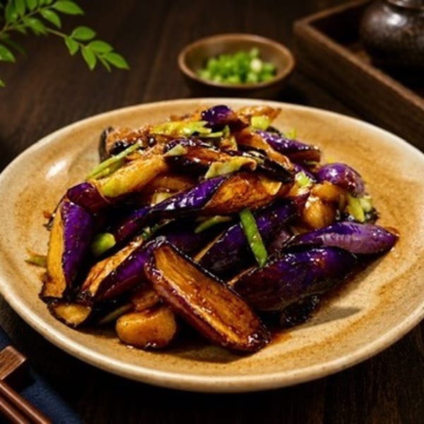 Sautéed eggplant with green onions and a glossy sauce on a rustic plate.