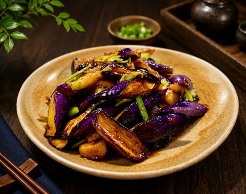 Sautéed eggplant with green onions and a glossy sauce on a rustic plate.