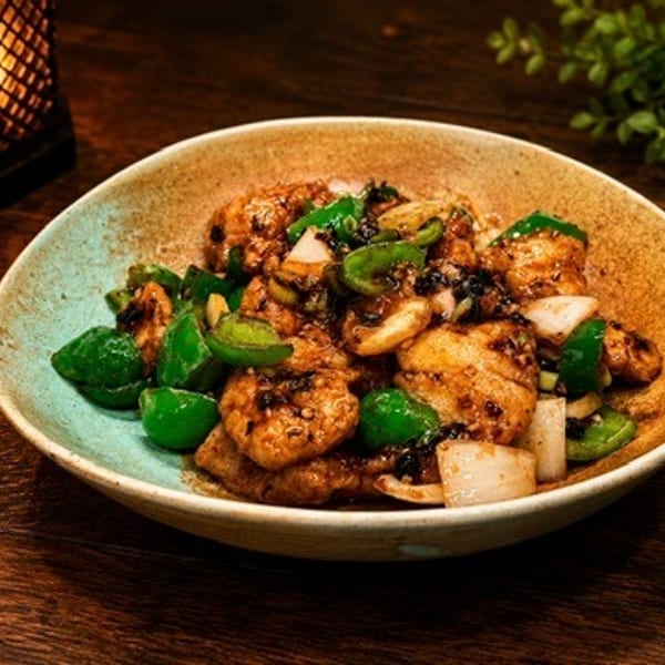 Stir-fried chicken with green bell peppers and onions in a rustic bowl on a wooden table.