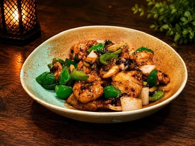 Stir-fried chicken with green bell peppers and onions in a rustic bowl on a wooden table.